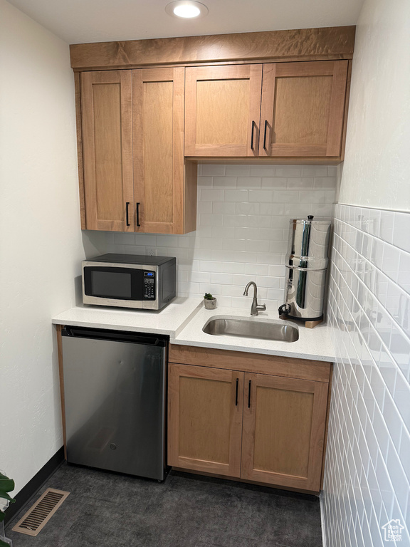 Kitchen with stainless steel microwave, fridge, a sink, light countertops, and brown cabinetry