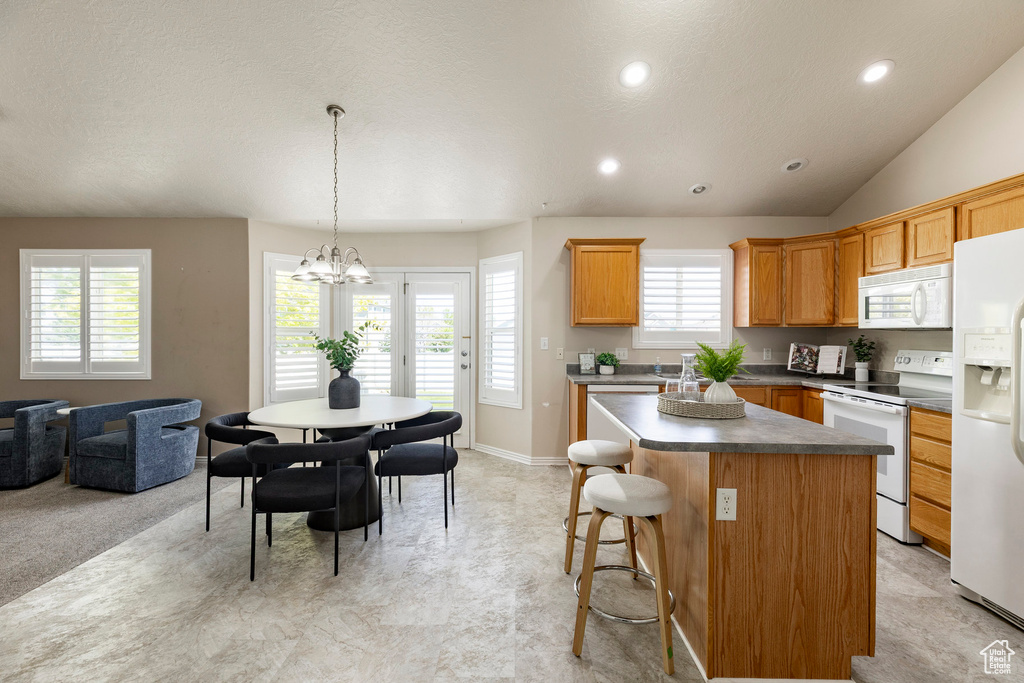 Kitchen featuring white appliances, a center island, a chandelier, healthy amount of natural light, and recessed lighting