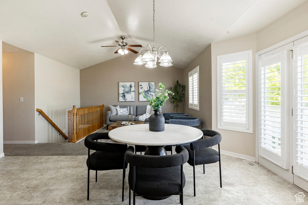 Dining room with lofted ceiling, light carpet, a chandelier, baseboards, and ceiling fan