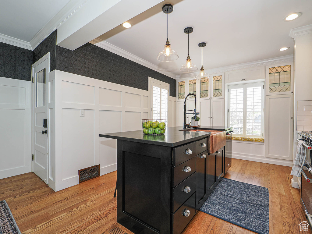 Kitchen with a decorative wall, ornamental molding, wallpapered walls, dark countertops, and dark cabinets