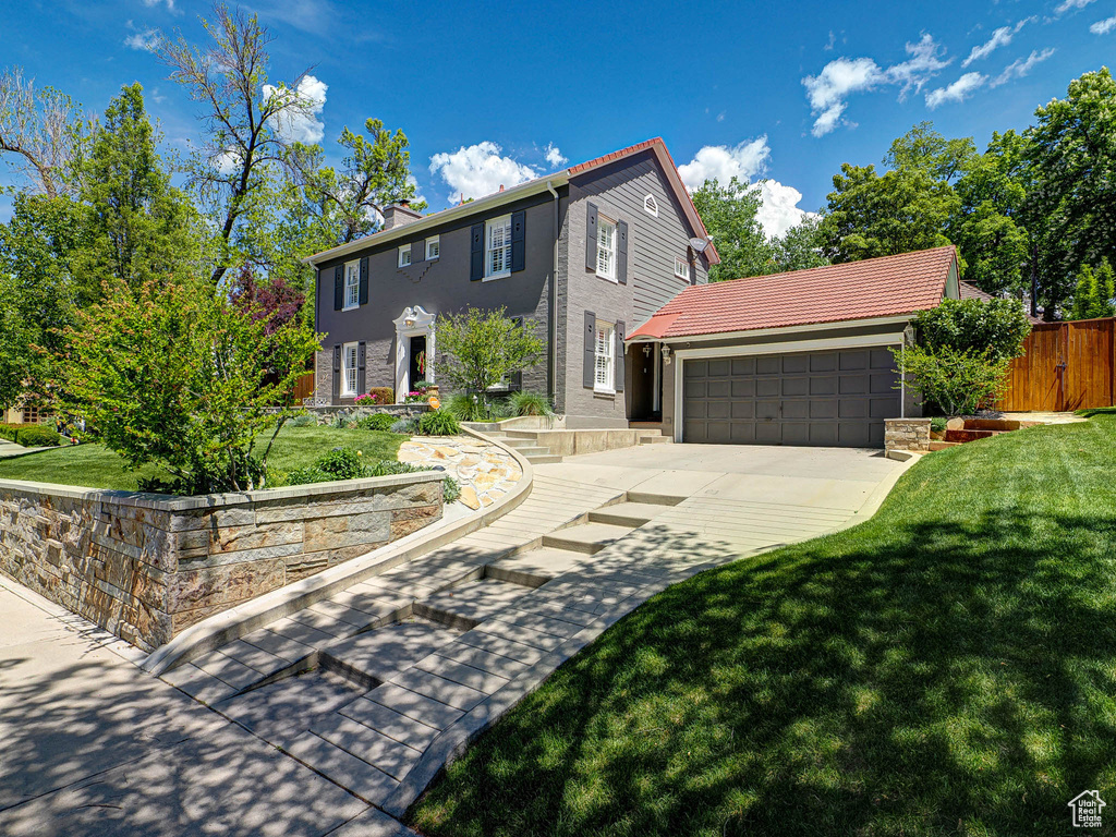 Colonial house with stucco siding, a garage, driveway, and a chimney