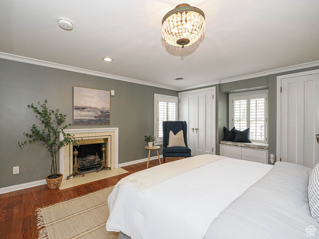 Bedroom with crown molding, wood finished floors, baseboards, two closets, and a fireplace