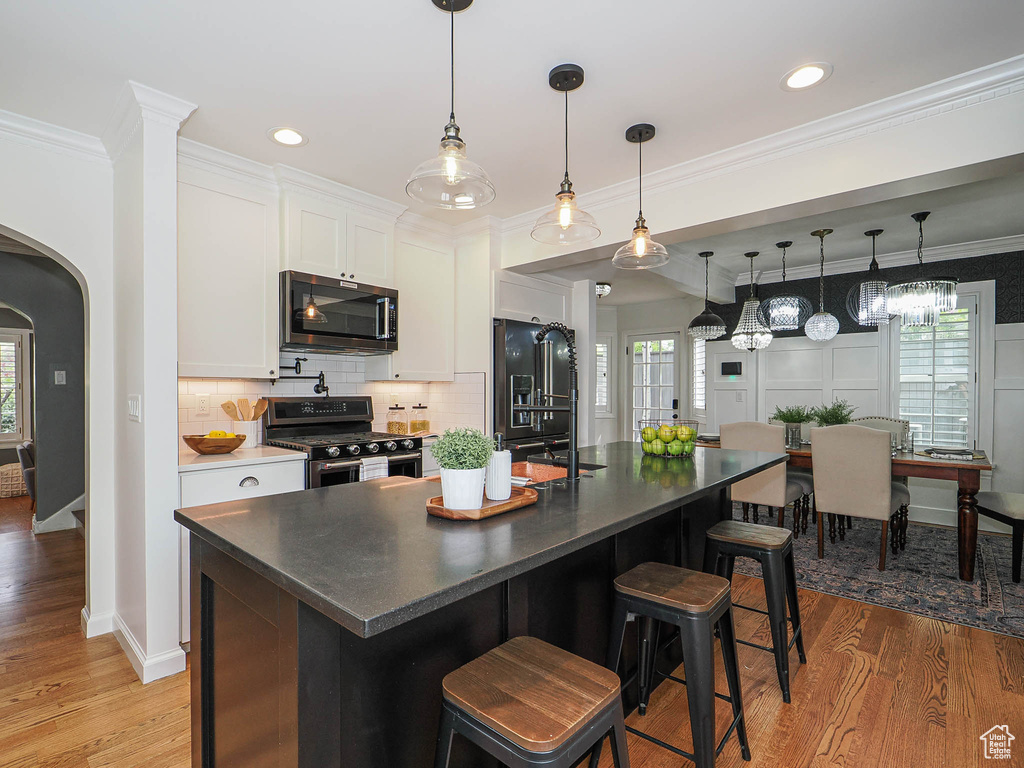 Kitchen featuring appliances with stainless steel finishes, arched walkways, white cabinets, backsplash, and light wood-type flooring