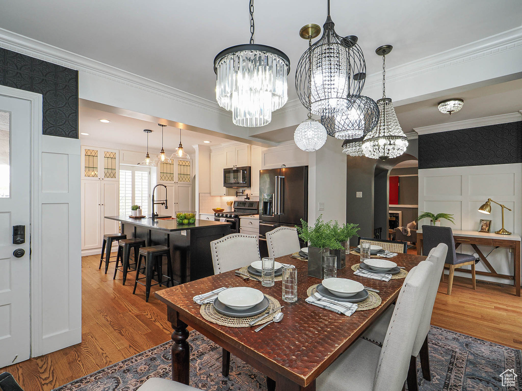 Dining area featuring a chandelier, wood finished floors, crown molding, arched walkways, and a decorative wall