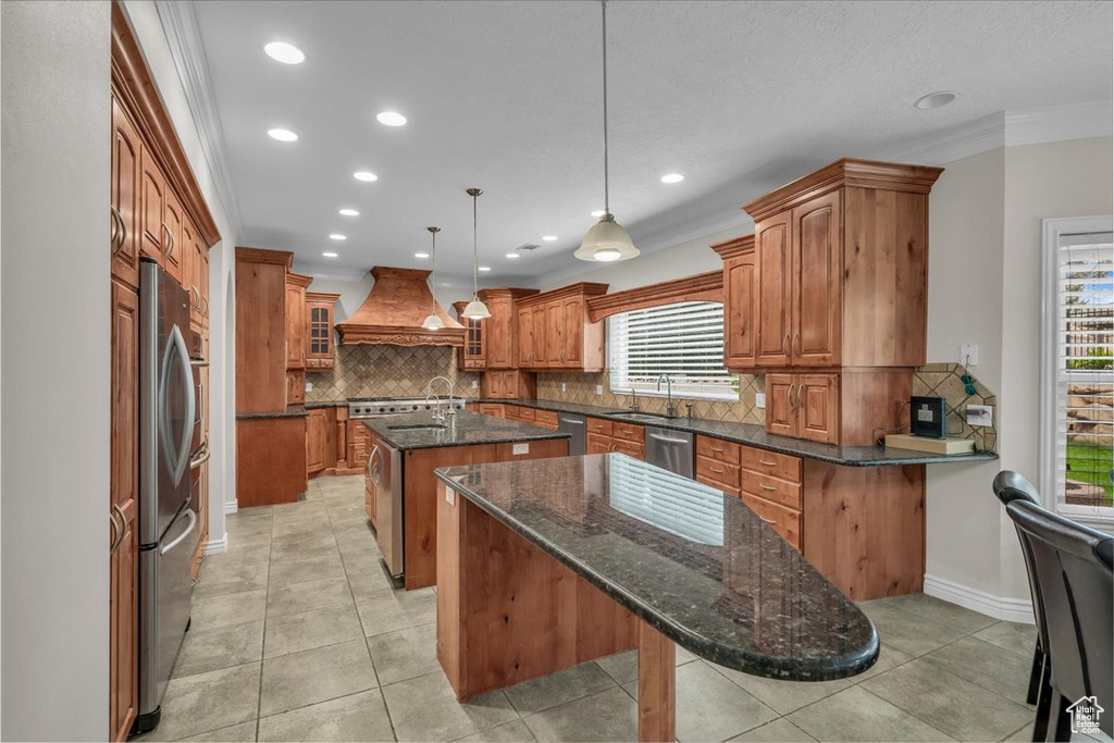 Kitchen with premium range hood, a center island with sink, brown cabinets, stainless steel appliances, and tasteful backsplash