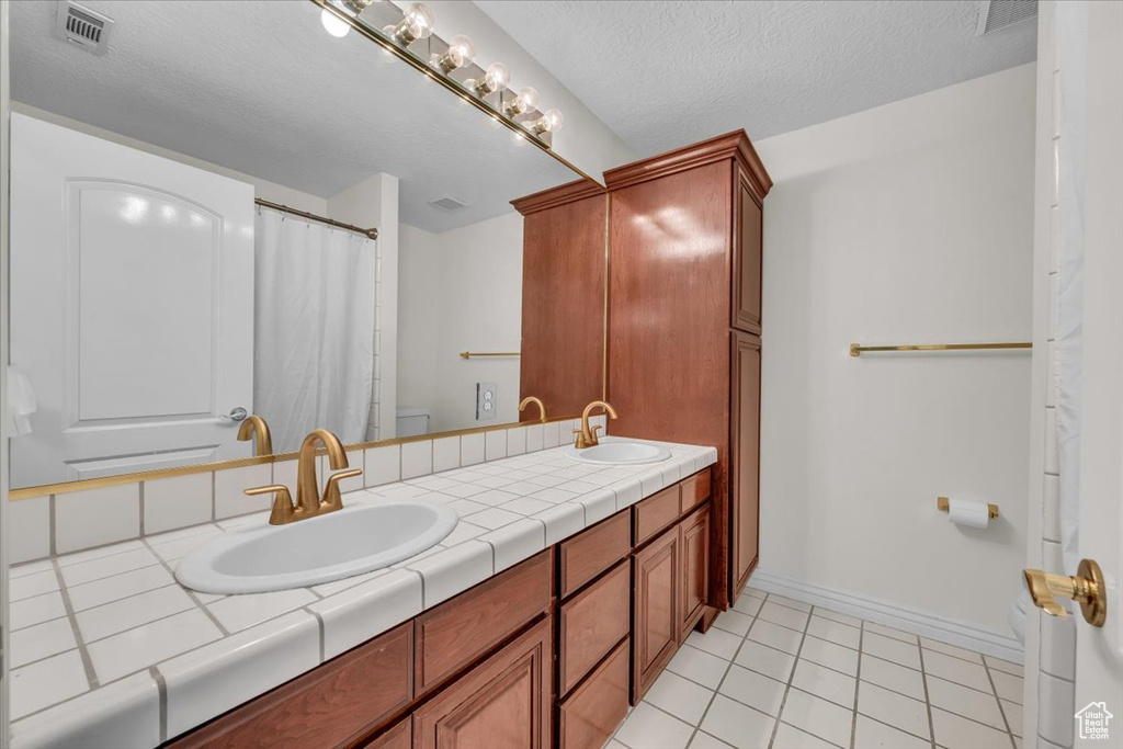Bathroom with toilet, tile patterned floors, baseboards, double vanity, and a textured ceiling