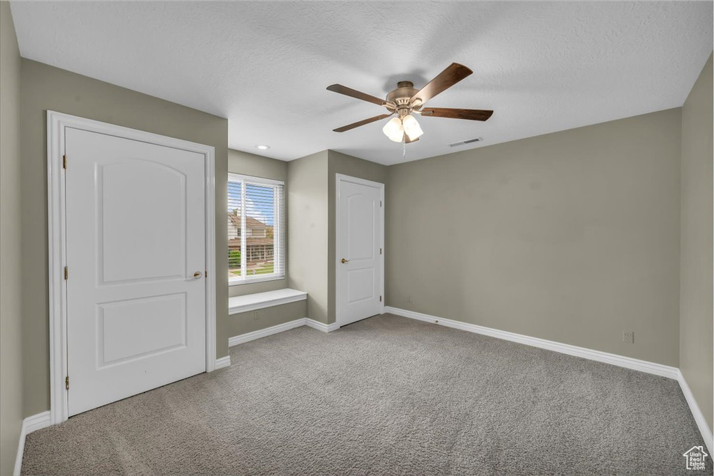 Unfurnished bedroom featuring carpet floors, baseboards, a textured ceiling, and a ceiling fan