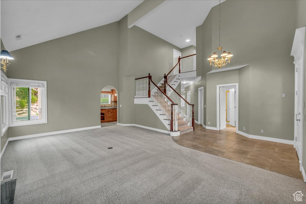 Unfurnished living room with high vaulted ceiling, a chandelier, baseboards, carpet, and arched walkways