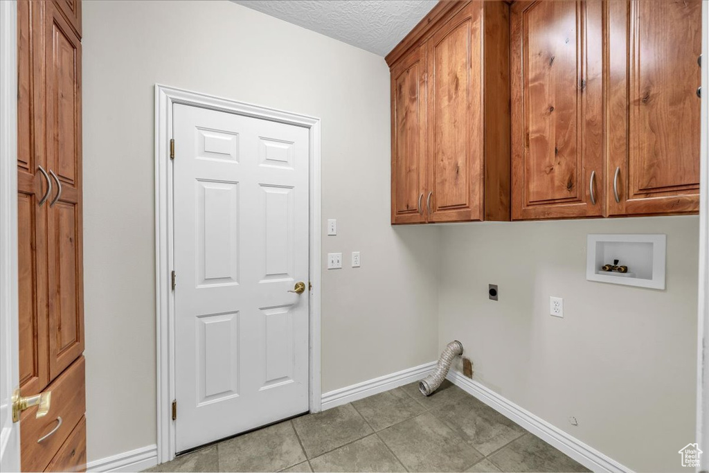 Laundry room with electric dryer hookup, hookup for a washing machine, cabinet space, baseboards, and light tile patterned floors