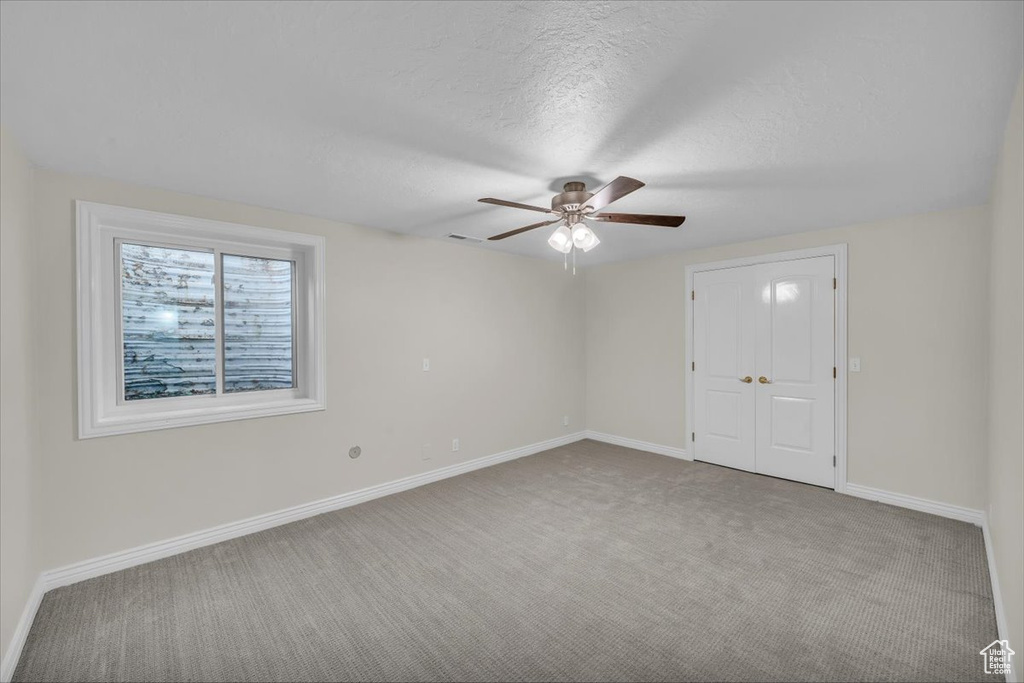 Empty room featuring carpet flooring, ceiling fan, baseboards, and a textured ceiling