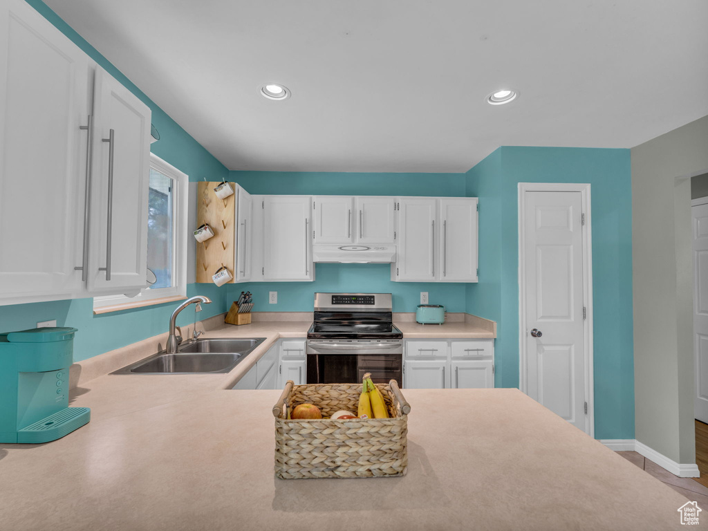 Kitchen with stainless steel electric range, a sink, under cabinet range hood, white cabinetry, and light countertops