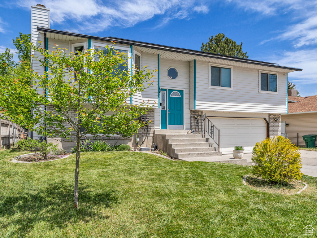 Bi-level home featuring an attached garage, a front lawn, a chimney, concrete driveway, and central AC unit