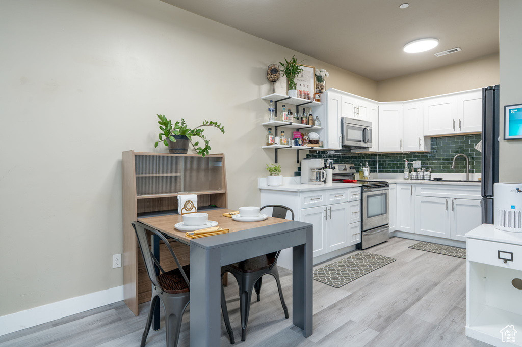 Kitchen with appliances with stainless steel finishes, light countertops, open shelves, and light wood-style floors