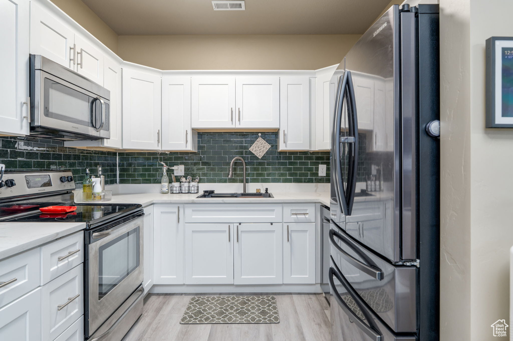 Kitchen featuring stainless steel appliances, a sink, white cabinetry, light countertops, and decorative backsplash