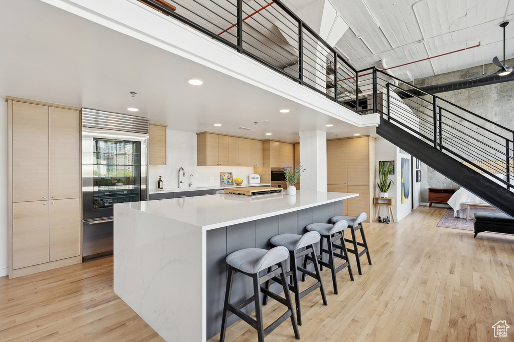 Kitchen with modern cabinets, appliances with stainless steel finishes, a sink, light brown cabinets, and light wood-type flooring