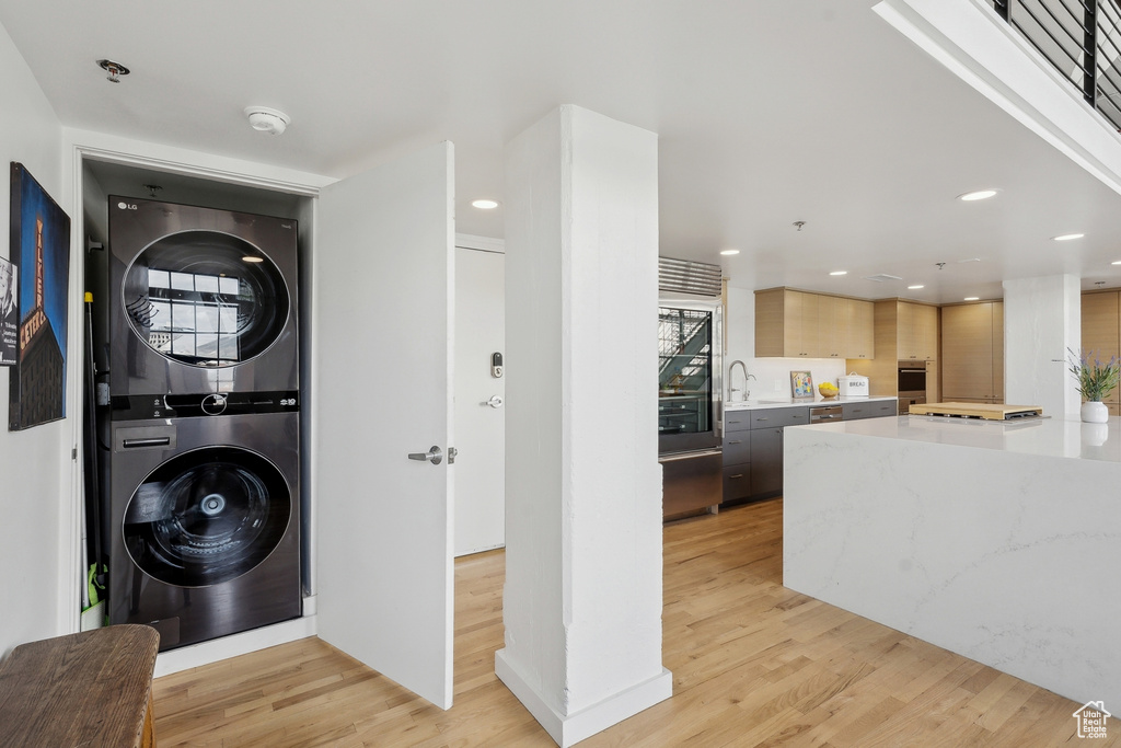 Laundry area with stacked washer / drying machine, light wood-style flooring, and recessed lighting