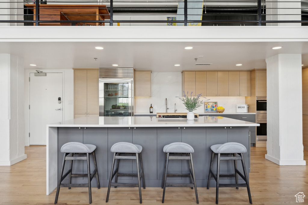 Kitchen featuring light wood-style floors, light countertops, a breakfast bar, recessed lighting, and a large island