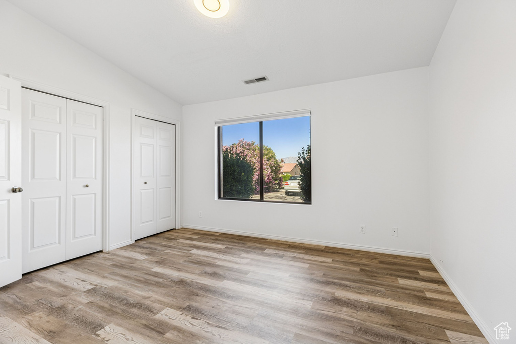 Unfurnished bedroom with two closets, wood finished floors, vaulted ceiling, and baseboards