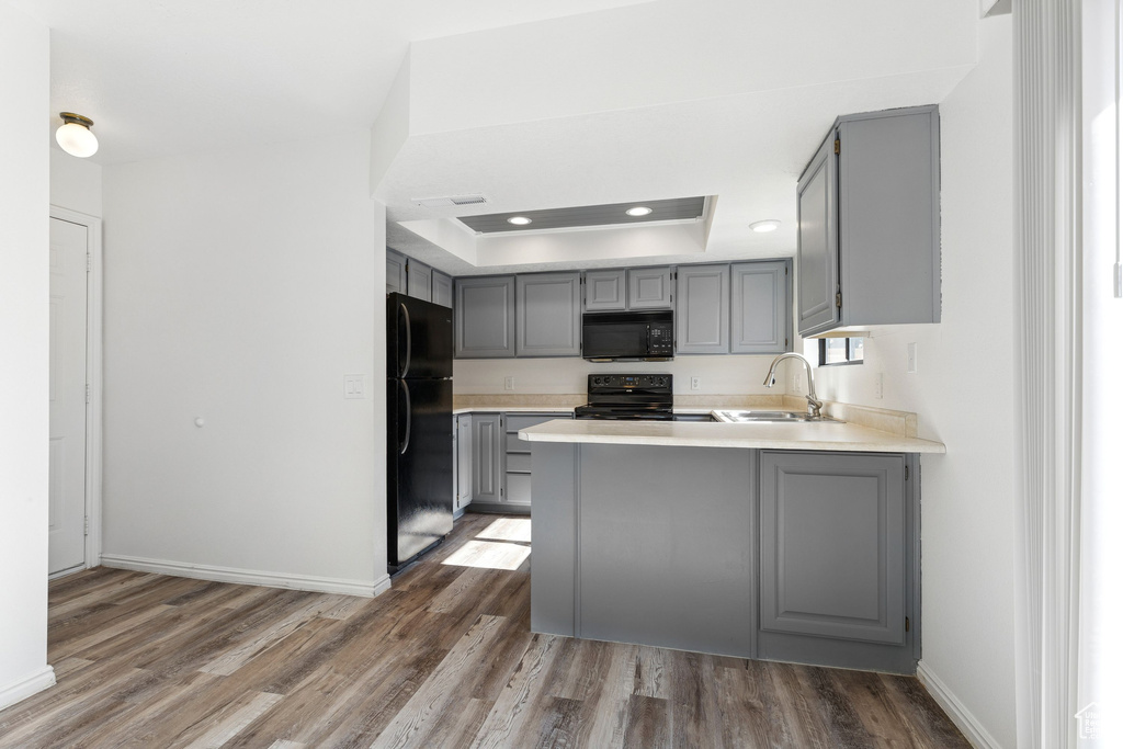 Kitchen featuring gray cabinets, black appliances, a sink, a tray ceiling, and a peninsula