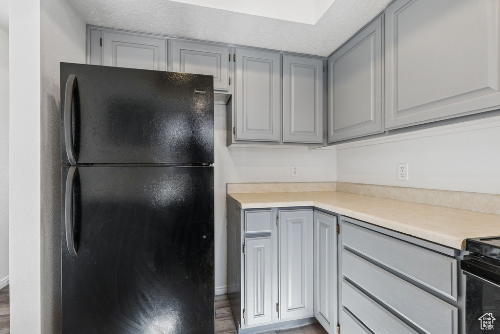 Kitchen with freestanding refrigerator, gray cabinets, light countertops, wood finished floors, and a skylight