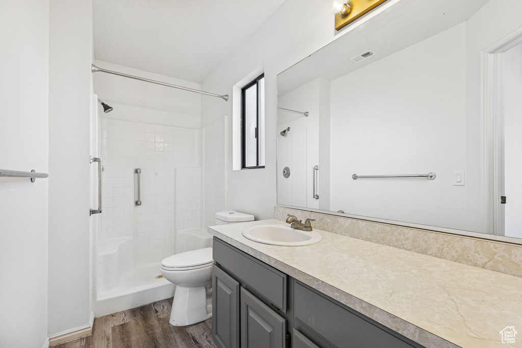 Bathroom featuring vanity, a tile shower, toilet, and wood finished floors