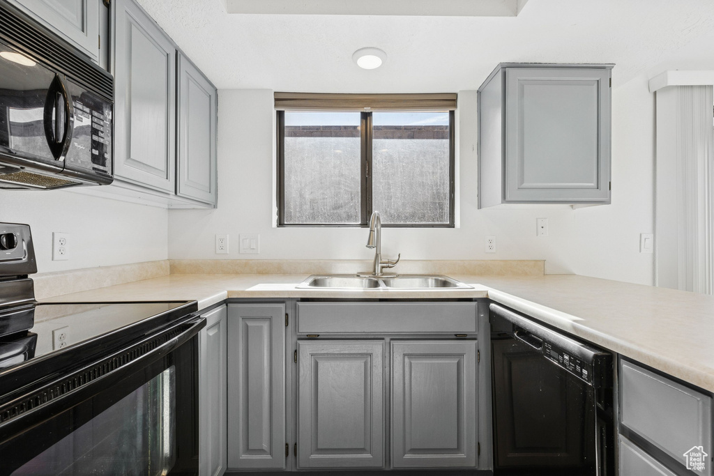 Kitchen featuring black appliances, gray cabinetry, a sink, and light countertops