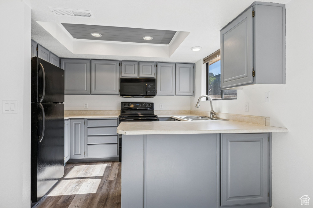 Kitchen with black appliances, gray cabinetry, a sink, a tray ceiling, and a peninsula