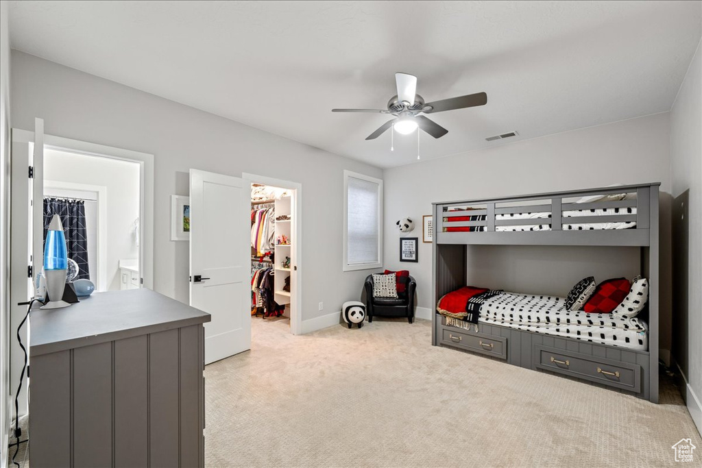 Bedroom with a walk in closet, light colored carpet, baseboards, a closet, and ceiling fan