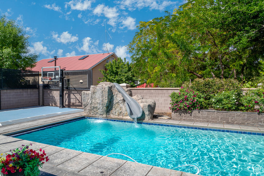 View of swimming pool with a water slide and a fenced backyard