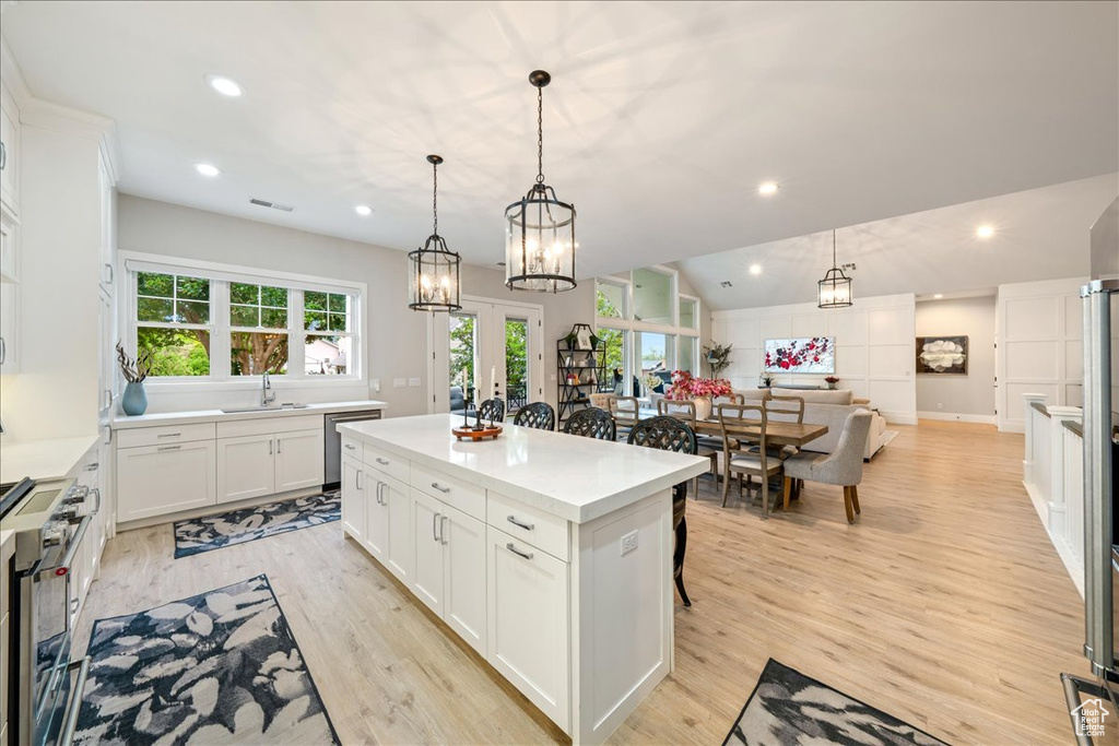 Kitchen featuring appliances with stainless steel finishes, a kitchen island, white cabinetry, light wood-style floors, and light countertops