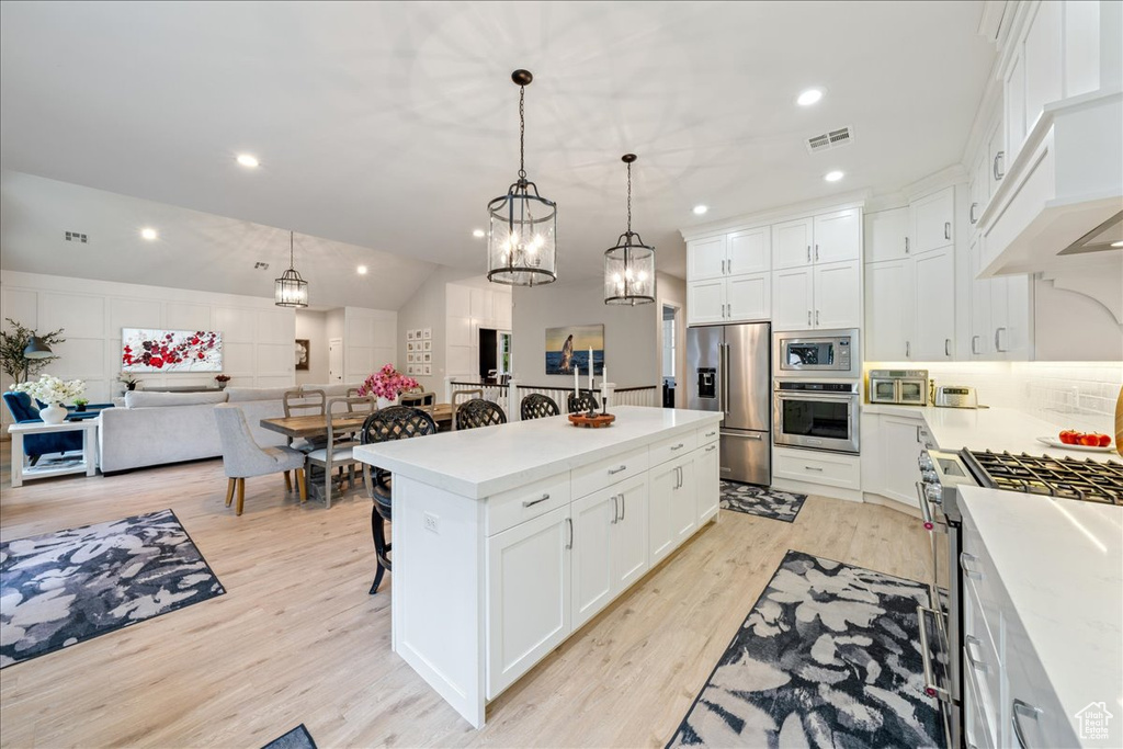Kitchen with appliances with stainless steel finishes, a kitchen bar, light wood-type flooring, light countertops, and recessed lighting