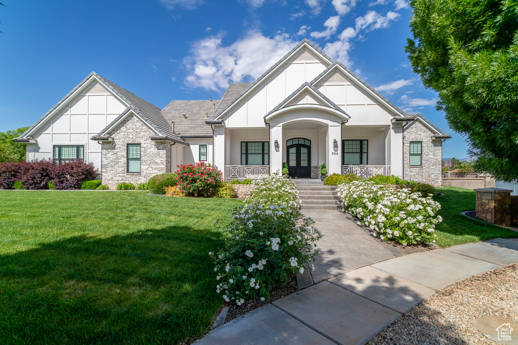 View of front of home with a porch, a front yard, stucco siding, french doors, and stone siding