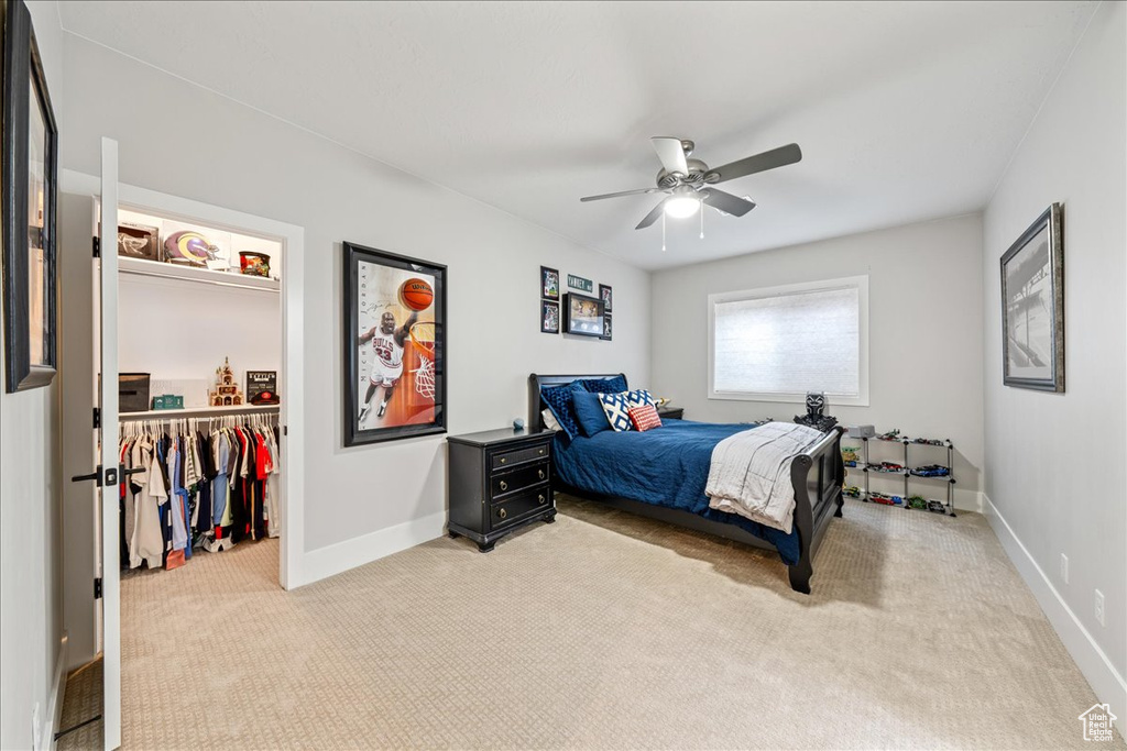 Bedroom with light colored carpet, a walk in closet, baseboards, a closet, and a ceiling fan
