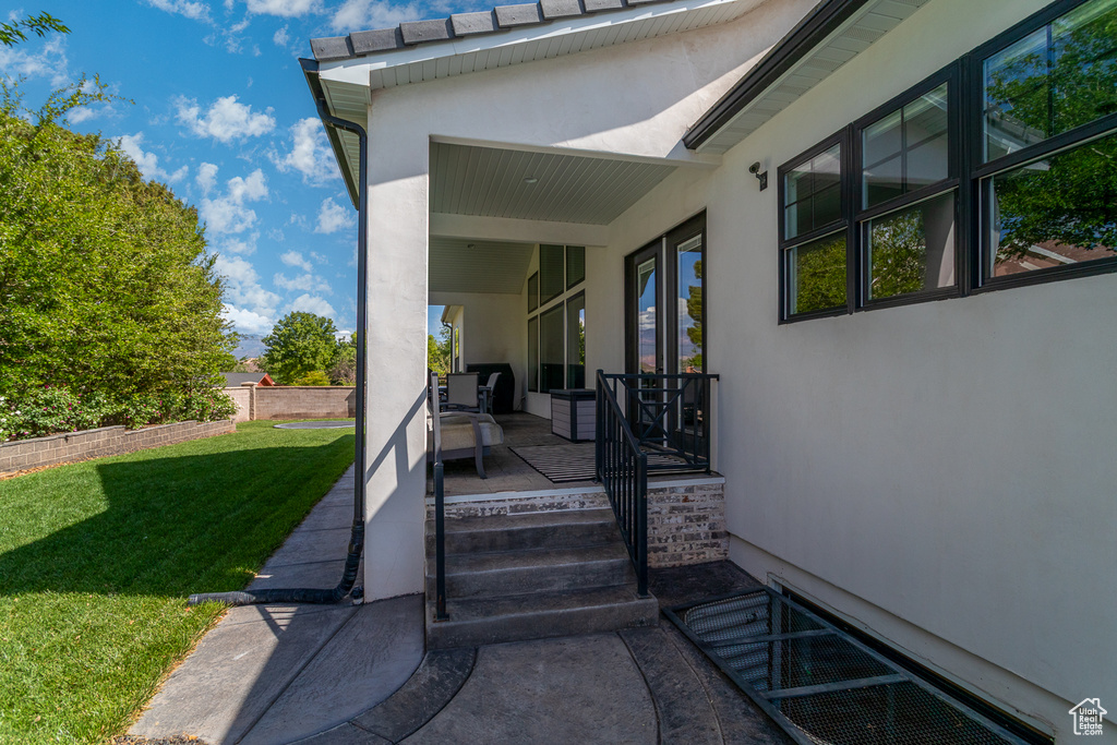 View of exterior entry with stucco siding and a yard