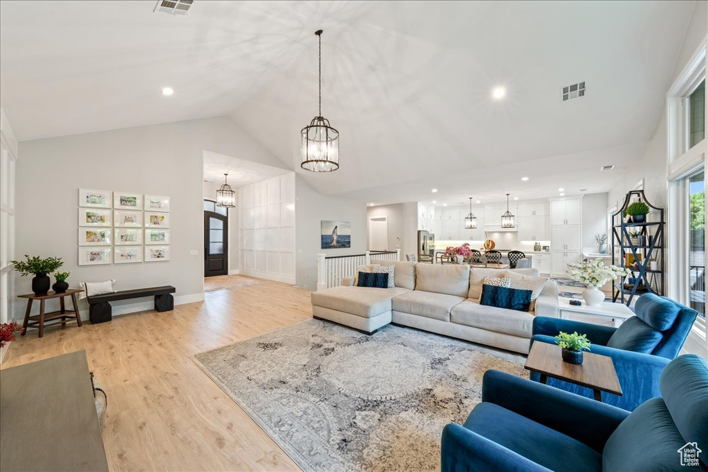 Living room with a chandelier, light wood-style flooring, high vaulted ceiling, recessed lighting, and baseboards