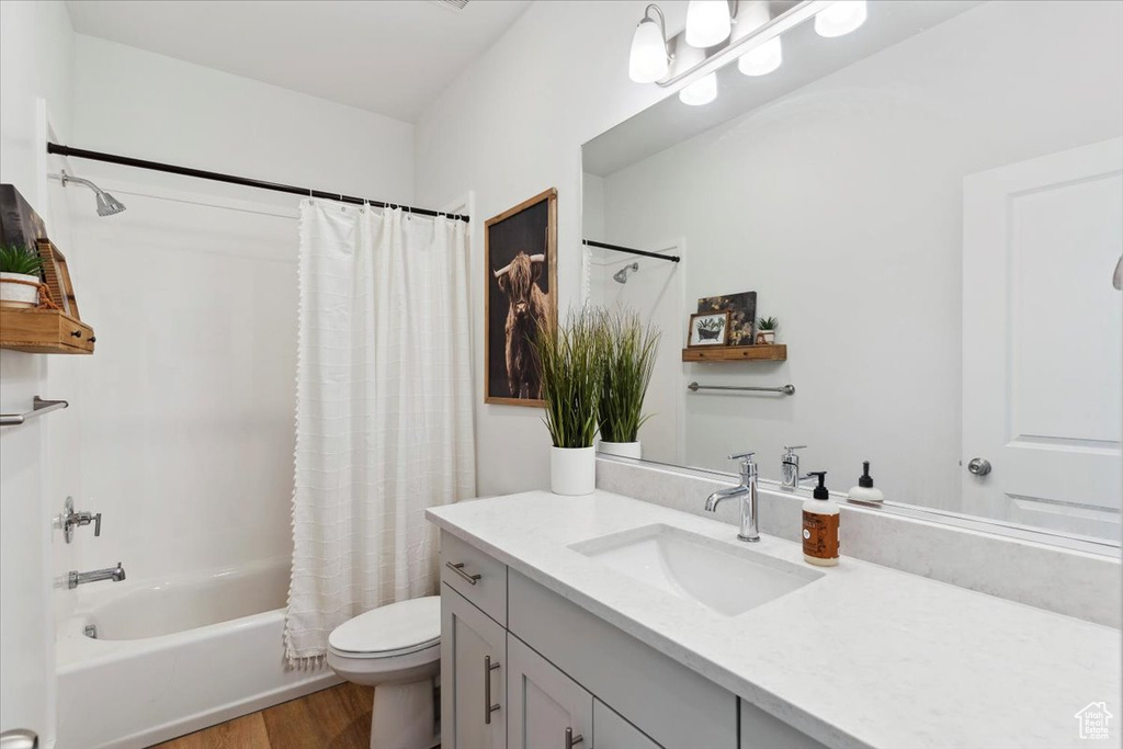 Bathroom with wood finished floors, toilet, vanity, and shower / bathtub combination with curtain