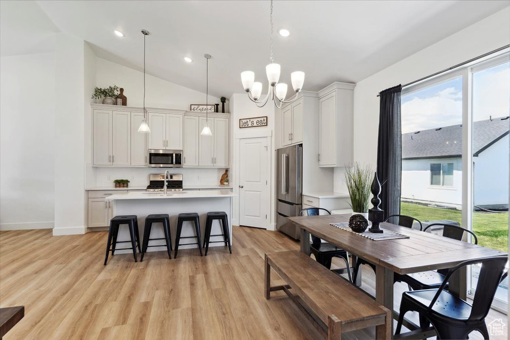 Dining space with light wood-type flooring, a chandelier, baseboards, recessed lighting, and high vaulted ceiling