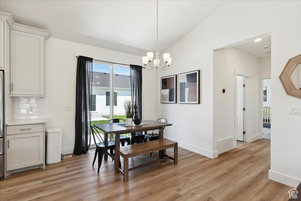 Dining area featuring a chandelier, light wood-style flooring, baseboards, and vaulted ceiling