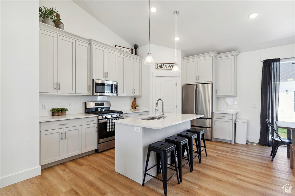 Kitchen featuring stainless steel appliances, a sink, a kitchen breakfast bar, decorative backsplash, and light countertops