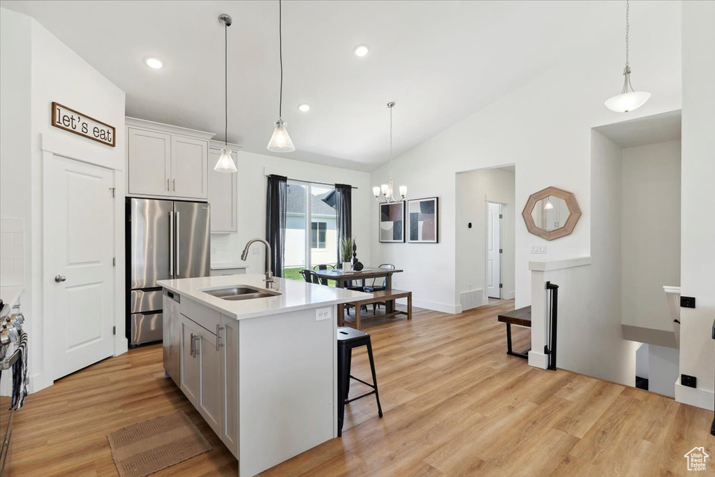 Kitchen featuring a sink, high end refrigerator, vaulted ceiling, light wood finished floors, and a center island with sink