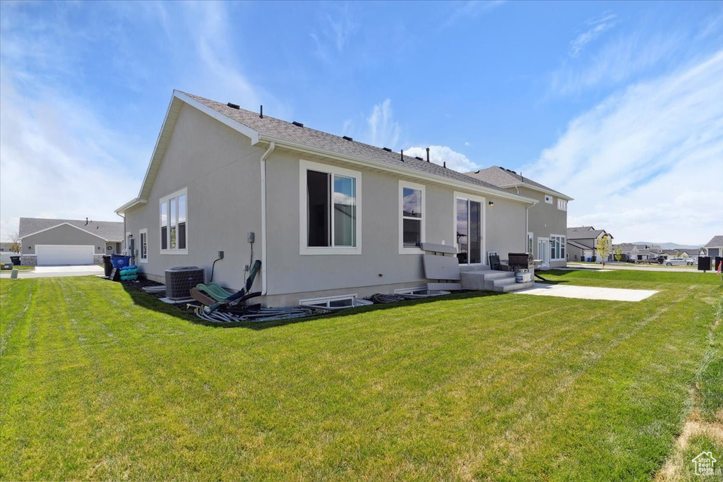 Back of house featuring stucco siding, central air condition unit, and a yard