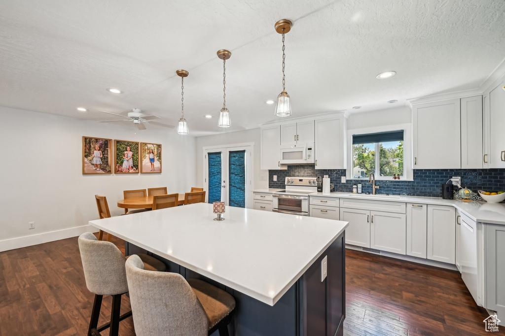 Kitchen with white microwave, range with electric stovetop, tasteful backsplash, a breakfast bar area, and recessed lighting