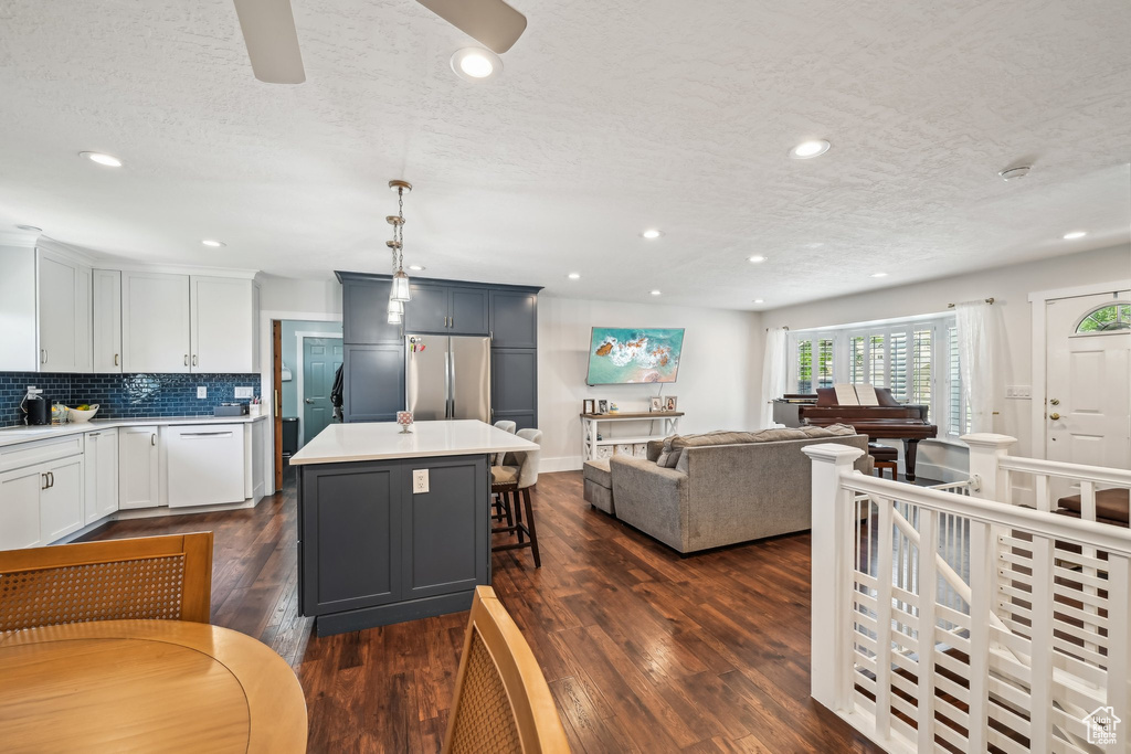 Kitchen with freestanding refrigerator, open floor plan, light countertops, a kitchen bar, and dishwasher