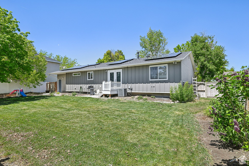 Rear view of property featuring board and batten siding, french doors, a wooden deck, roof mounted solar panels, and cooling unit