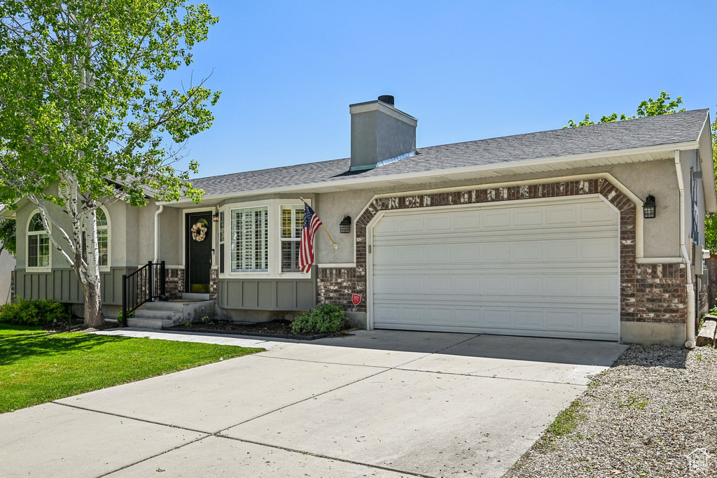 Ranch-style house with brick siding, a garage, driveway, a front yard, and stucco siding