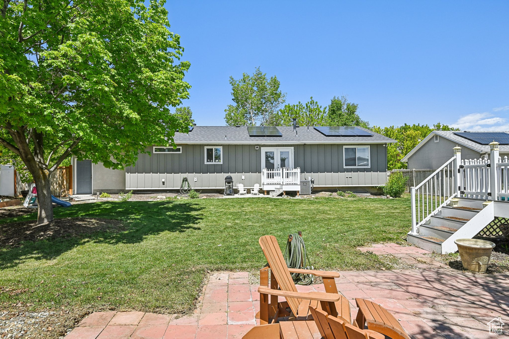 Rear view of house with board and batten siding, a patio, roof mounted solar panels, french doors, and a yard