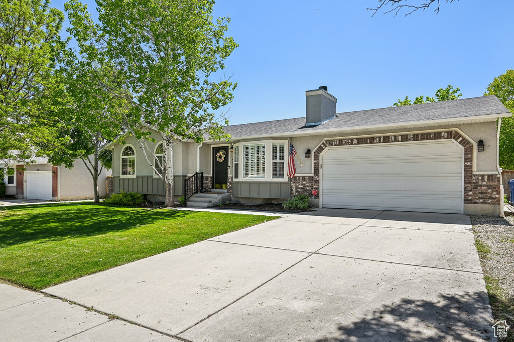 Single story home featuring a garage, driveway, a front yard, brick siding, and a chimney