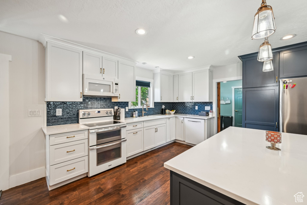 Kitchen with white appliances, a sink, light countertops, dark wood-style flooring, and recessed lighting