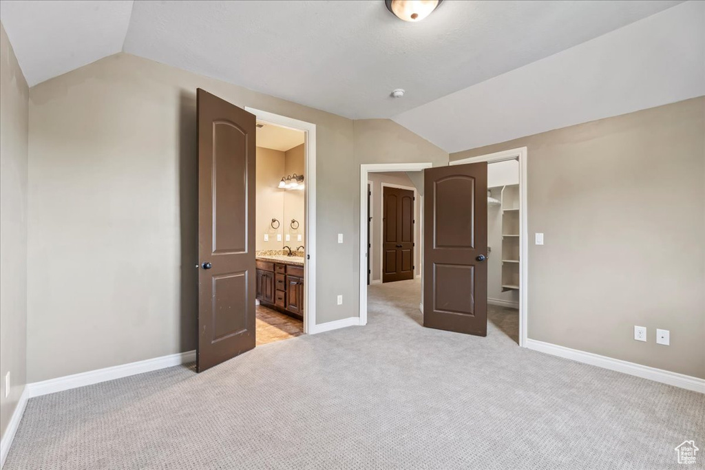 Unfurnished bedroom featuring vaulted ceiling, light colored carpet, a sink, baseboards, and a closet