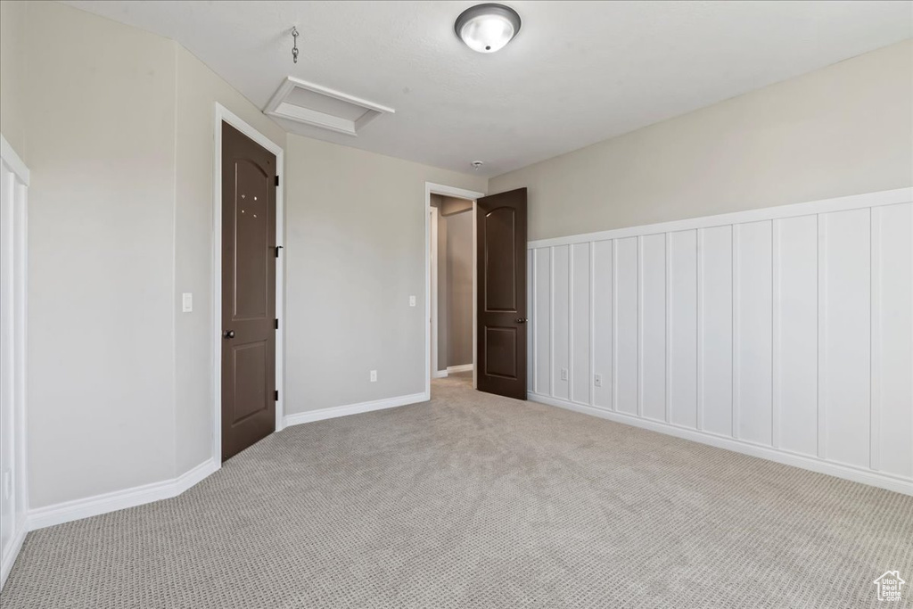 Unfurnished bedroom with attic access, light carpet, and baseboards